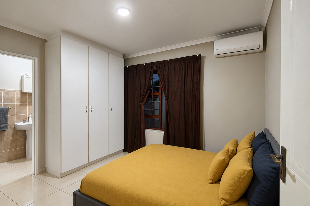 A well-maintained bedroom featuring built-in wardrobes, split-system air conditioning, tiled flooring, and an en-suite bathroom.