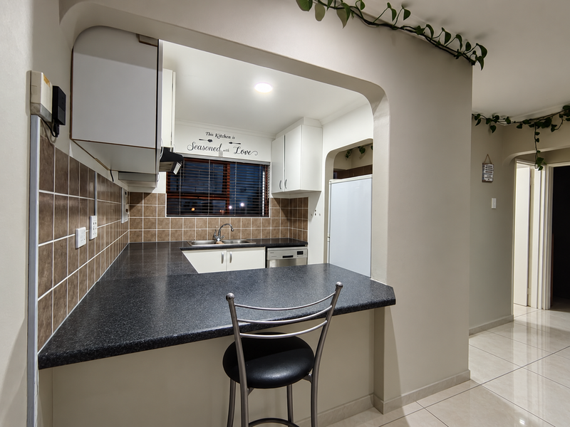A functional kitchen featuring dark laminate countertops, tiled backsplash, built-in cabinetry, and a breakfast bar opening into the adjacent living space.