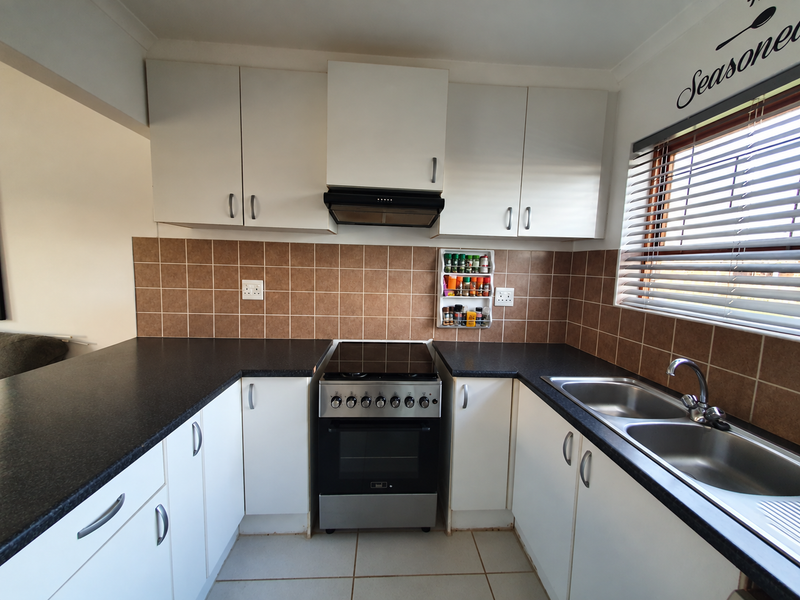 A functional kitchen featuring white cabinetry, dark laminate countertops, a stainless steel double sink, and a freestanding stove with an extractor fan.