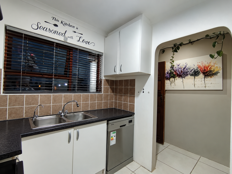 A functional kitchen area featuring a double bowl sink, tiled backsplash, built-in cabinetry, and an integrated dishwasher with neutral finishes.