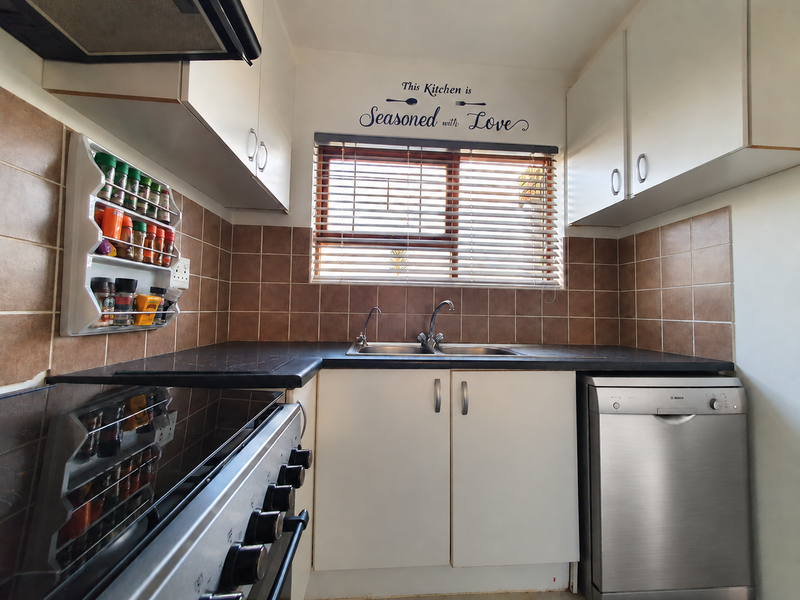 A functional kitchen featuring white cabinetry, dark countertops, a double sink, tiled backsplash, and integrated dishwasher, providing a practical workspace.