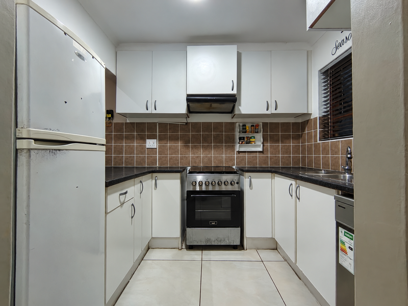 Compact kitchen featuring white cabinetry, dark laminate countertops, tiled backsplash, and a freestanding oven with extractor fan.