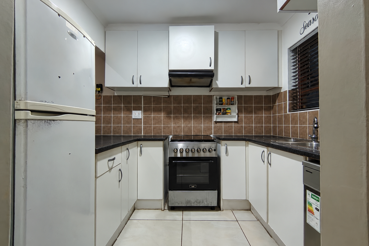 Compact kitchen featuring white cabinetry, dark laminate countertops, tiled backsplash, and a freestanding oven with extractor fan.