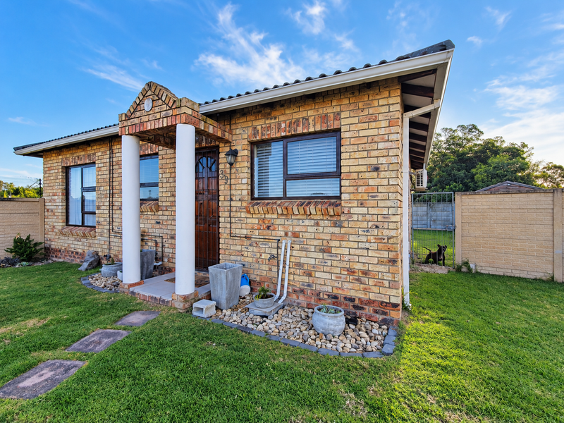 A well-maintained single-story face brick home featuring a covered entrance porch with decorative columns, aluminium window frames, and a neat surrounding garden.