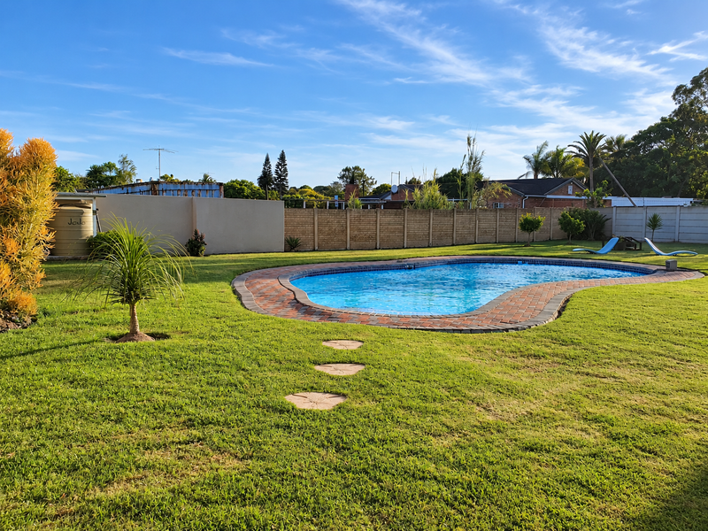 A well-maintained backyard featuring a swimming pool with brick coping, surrounded by a lush lawn and secure boundary walling.