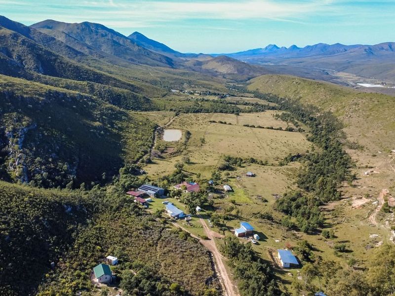 An aerial view of a rural farm property nestled in a valley, featuring multiple outbuildings, solar installations, and expansive grazing land.