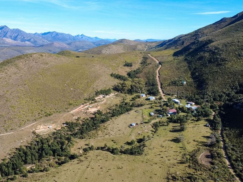 An aerial view of the farm property showcasing the expansive landscape, surrounding mountains, and the access road leading to the homestead.