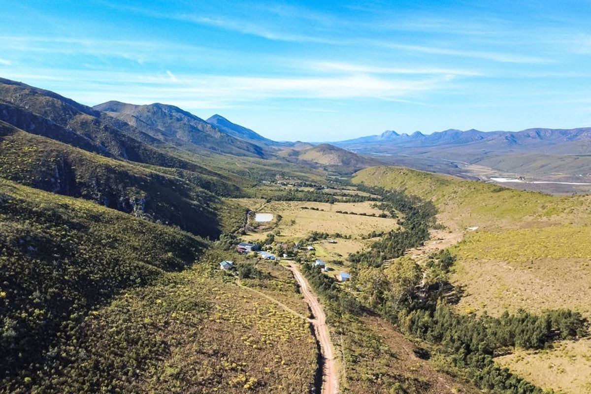 An expansive aerial view of a rural farm property nestled within a scenic mountain valley, featuring a dirt access road and natural landscape.