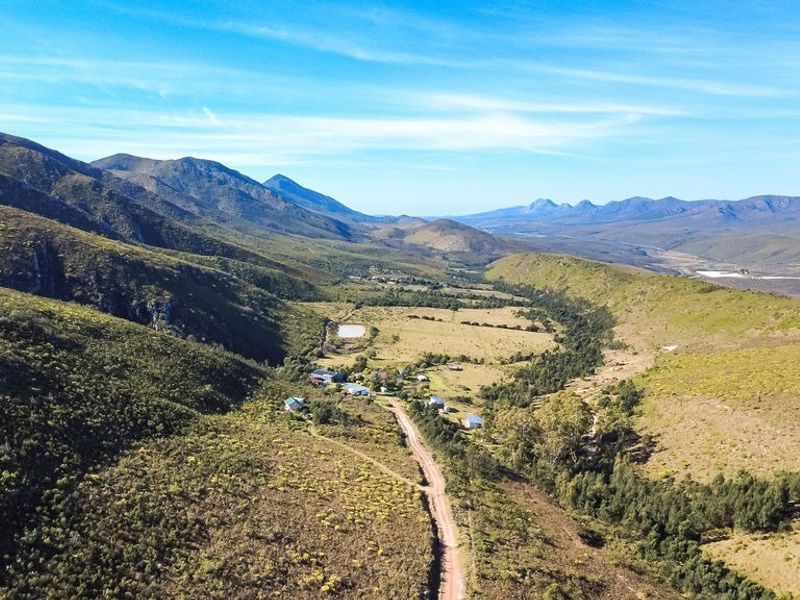 An expansive aerial view of a rural farm property nestled within a scenic mountain valley, featuring a dirt access road and natural landscape.