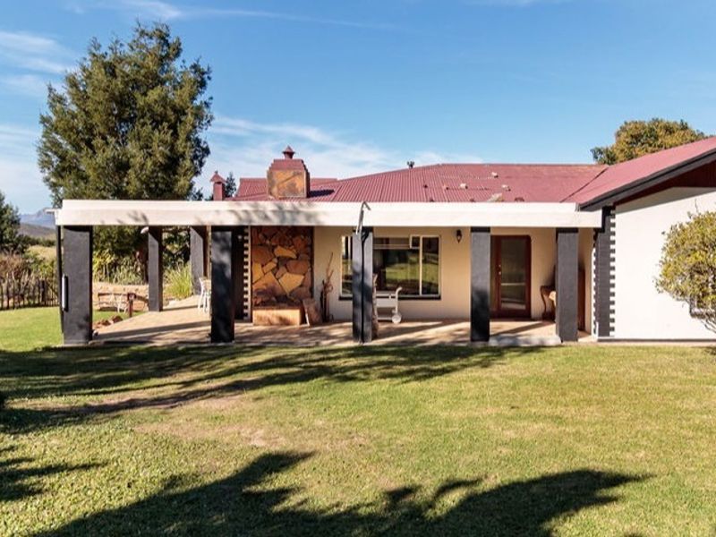 Rear view of the farmhouse featuring a spacious covered patio with a stone-clad fireplace, overlooking a well-maintained garden and surrounding landscape.