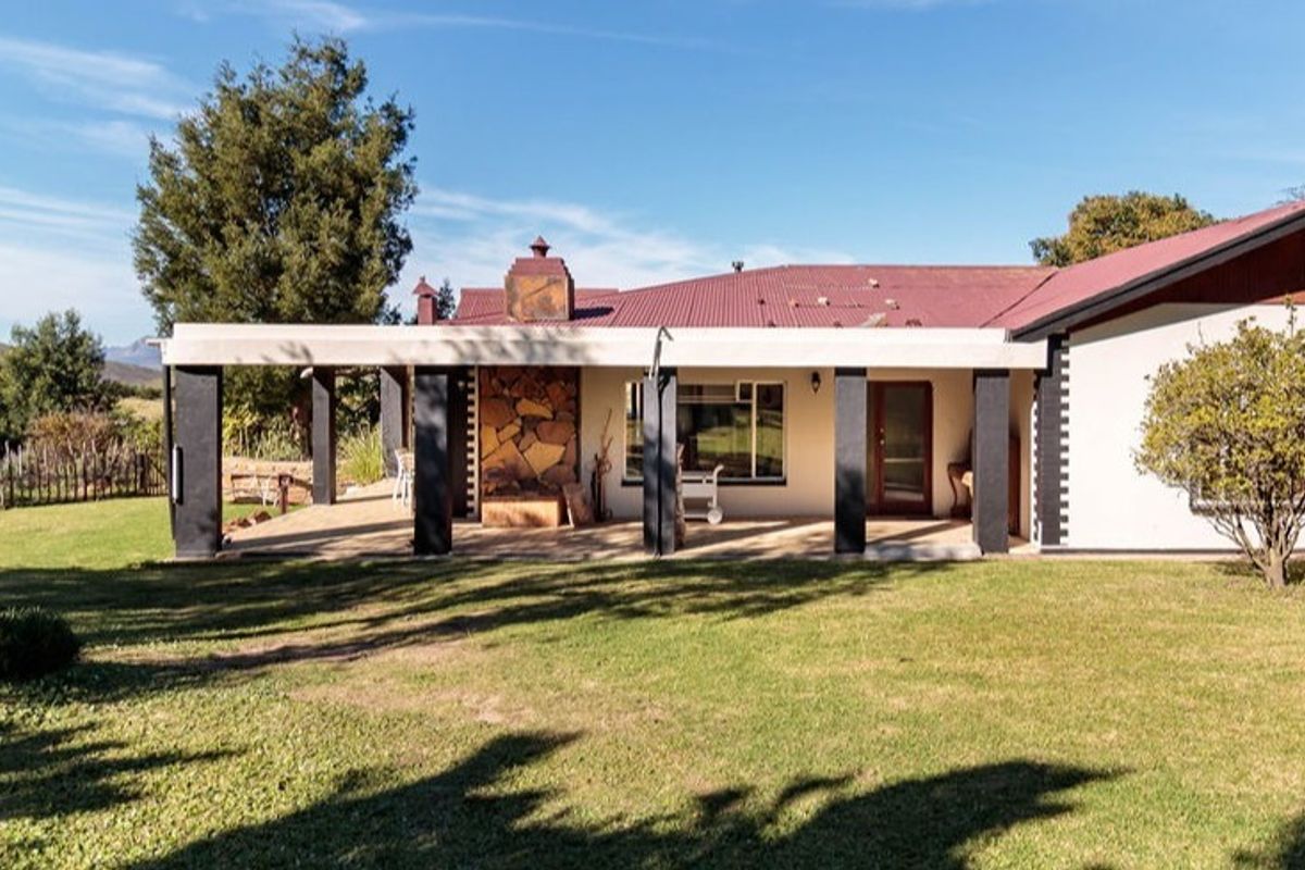 Rear view of the farmhouse featuring a spacious covered patio with a stone-clad fireplace, overlooking a well-maintained garden and surrounding landscape.