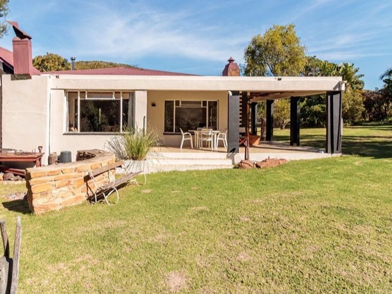 Rear view of the farmhouse featuring a covered patio area, stone garden wall, and established lawn in a rural setting.