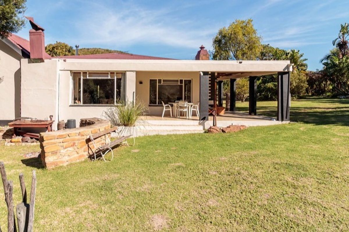 Rear view of the farmhouse featuring a covered patio area, stone garden wall, and established lawn in a rural setting.