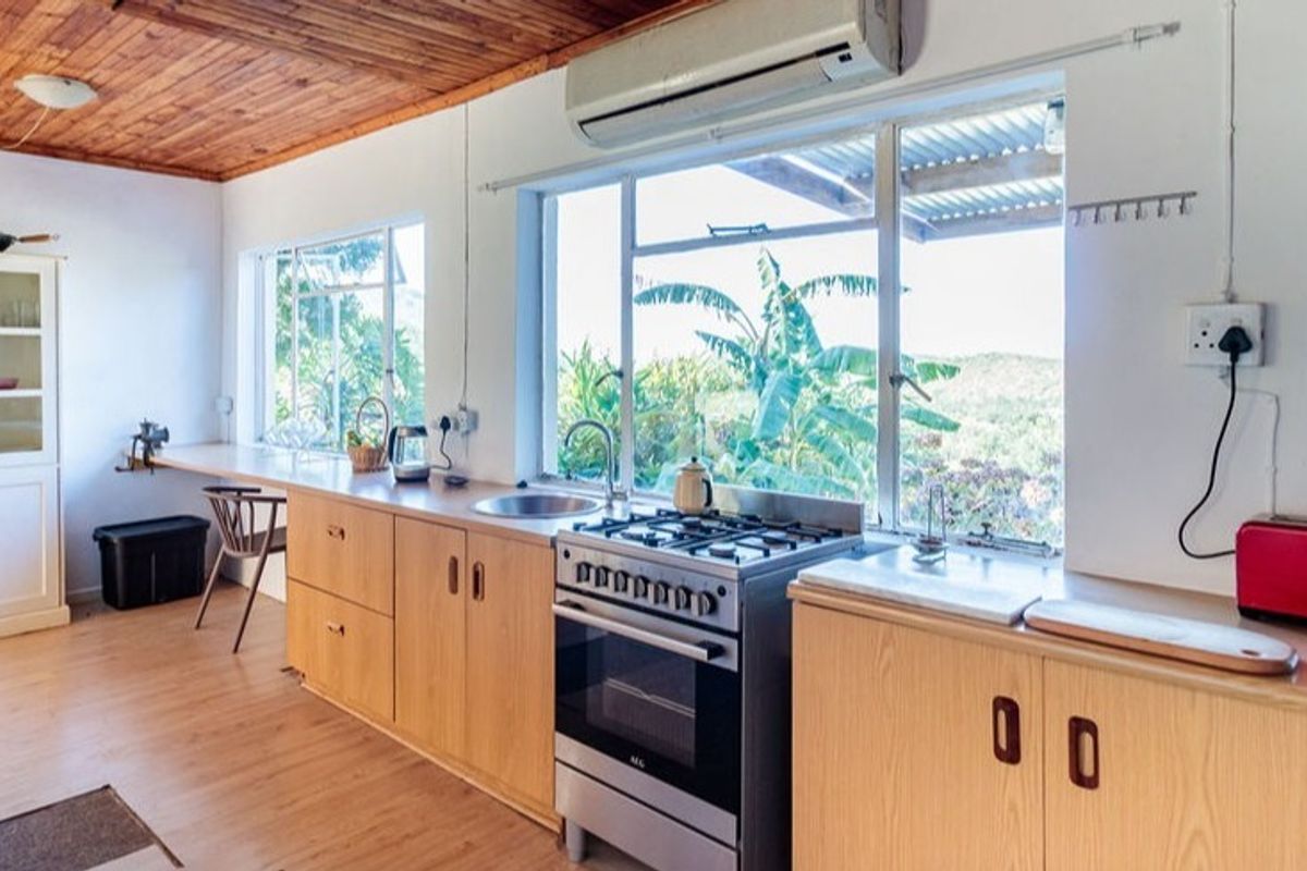 A functional kitchen featuring timber ceilings, light wood cabinetry, a gas stove, and large windows providing natural light and scenic views.