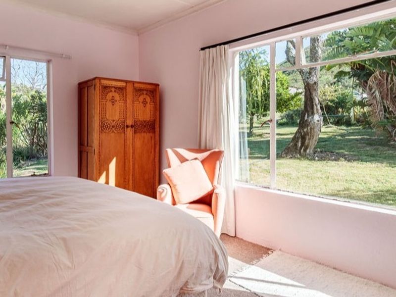 A bright bedroom featuring large windows that provide ample natural light and views of the surrounding garden.