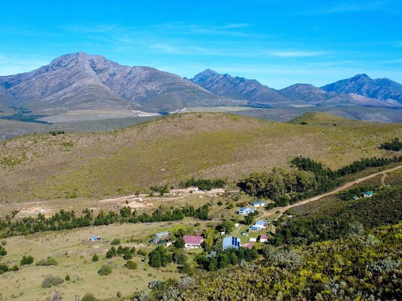 An expansive aerial view of a rural farm property nestled within a scenic mountain landscape, showcasing the surrounding terrain and access roads.