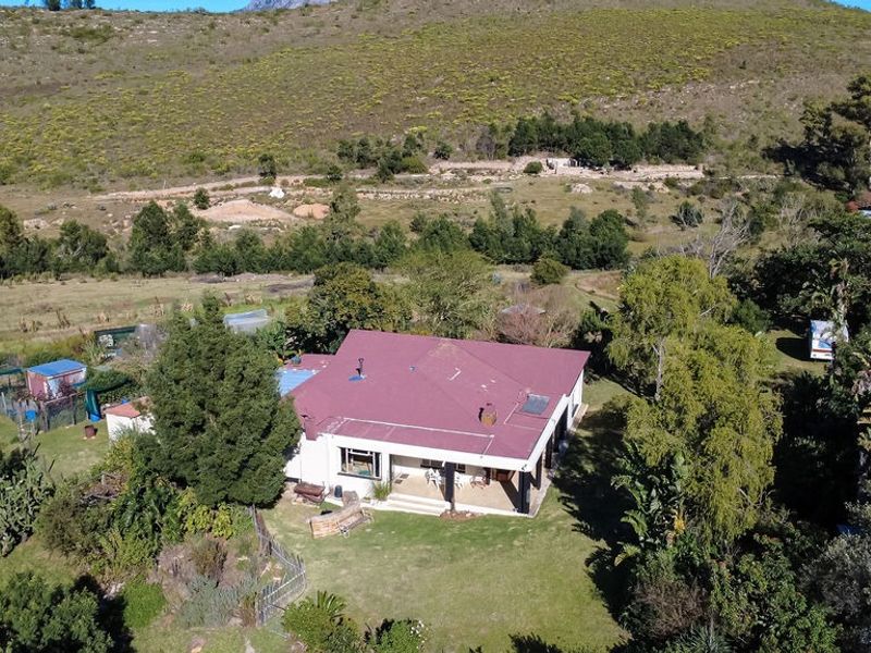 Aerial view of a farm property featuring a main dwelling with a metal roof, covered patio, and surrounding garden area set against a mountainous landscape.