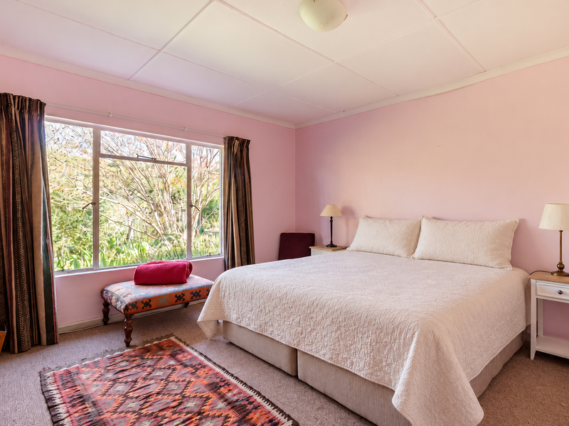 A spacious bedroom featuring a large window with garden views, neutral carpeting, and a classic tiled ceiling finish.