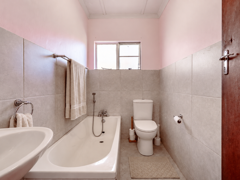 A functional bathroom featuring a bathtub, toilet, and pedestal basin with neutral wall tiling and pink painted upper walls.