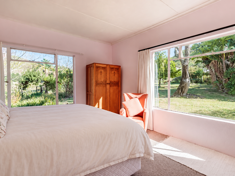 A bright bedroom featuring large windows that provide ample natural light and views of the surrounding garden.
