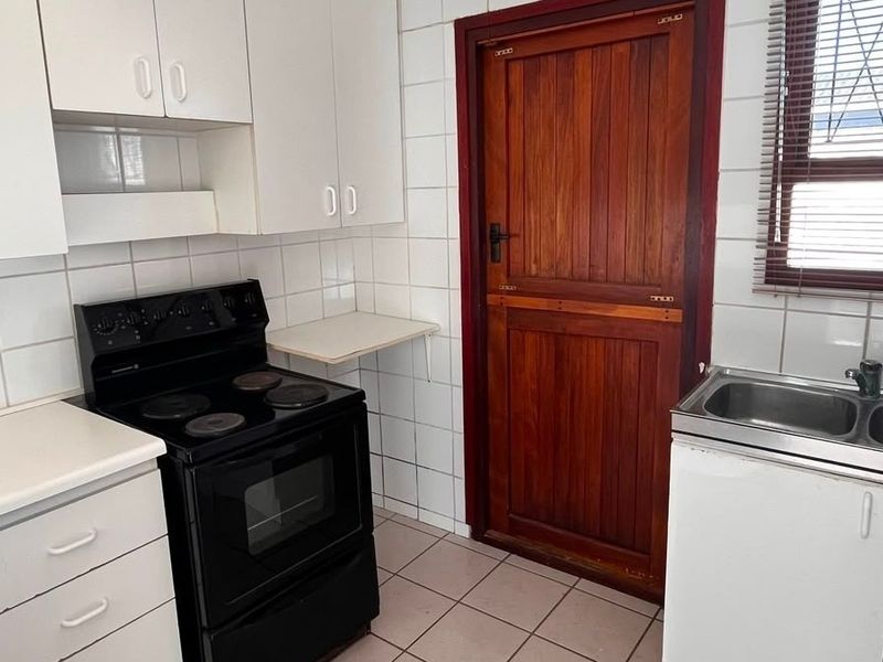 A functional kitchen featuring white cabinetry, tiled splashbacks, a double sink, and a freestanding stove, with direct access to an exterior timber door.