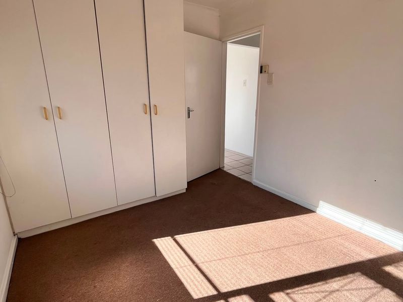 A vacant bedroom featuring built-in cupboards, a ceiling fan, and carpeted flooring, offering a blank canvas for potential updates.