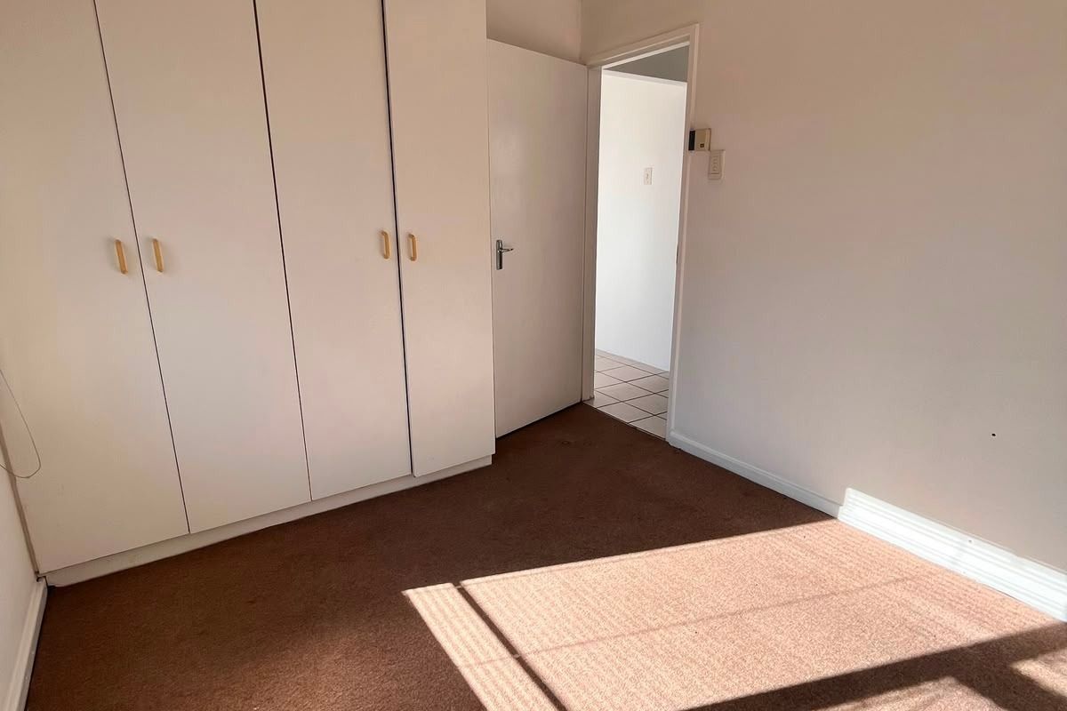A vacant bedroom featuring built-in cupboards, a ceiling fan, and carpeted flooring, offering a blank canvas for potential updates.