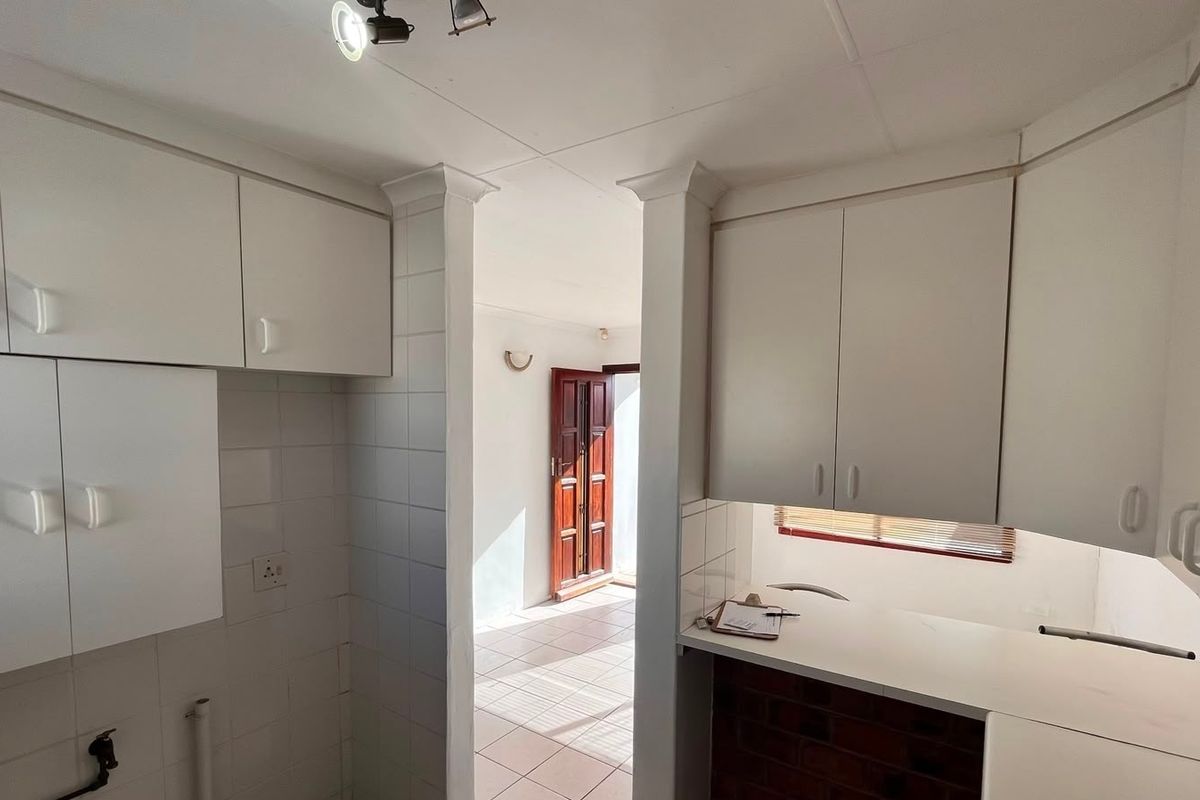 A functional kitchen space featuring white built-in cabinetry, tiled splashbacks, and a clean countertop, leading through to an adjacent living area.