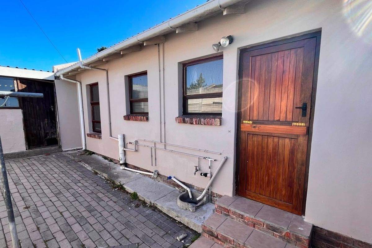 Rear exterior view of the property featuring a timber door, brick paving, and exposed external plumbing fixtures.