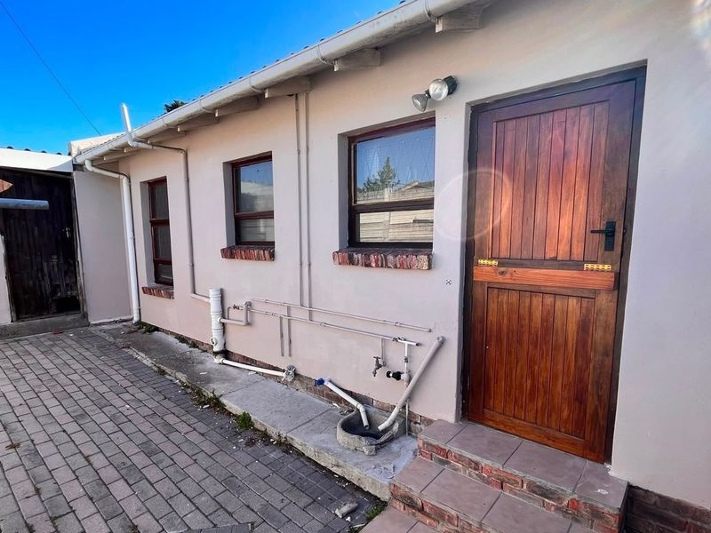 Rear exterior view of the property featuring a timber door, brick paving, and exposed external plumbing fixtures.