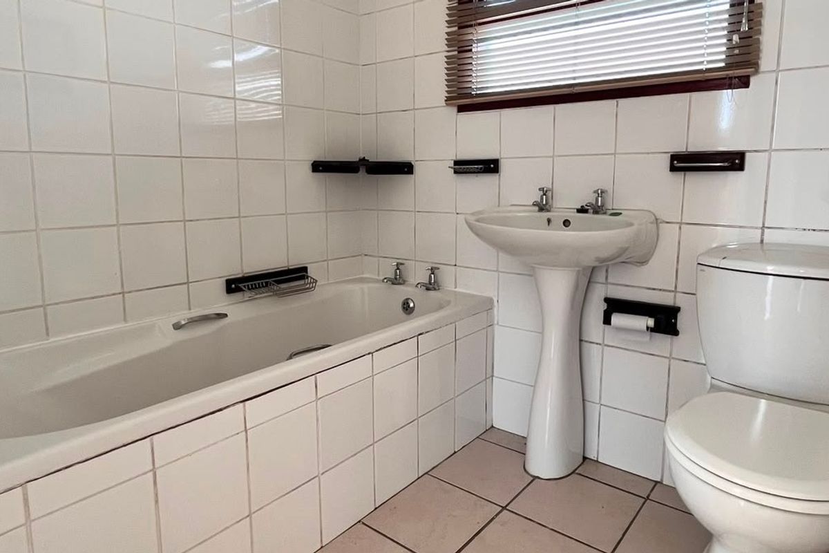A functional bathroom featuring a built-in bathtub, pedestal sink, and toilet, finished with white wall tiles and neutral floor tiling.