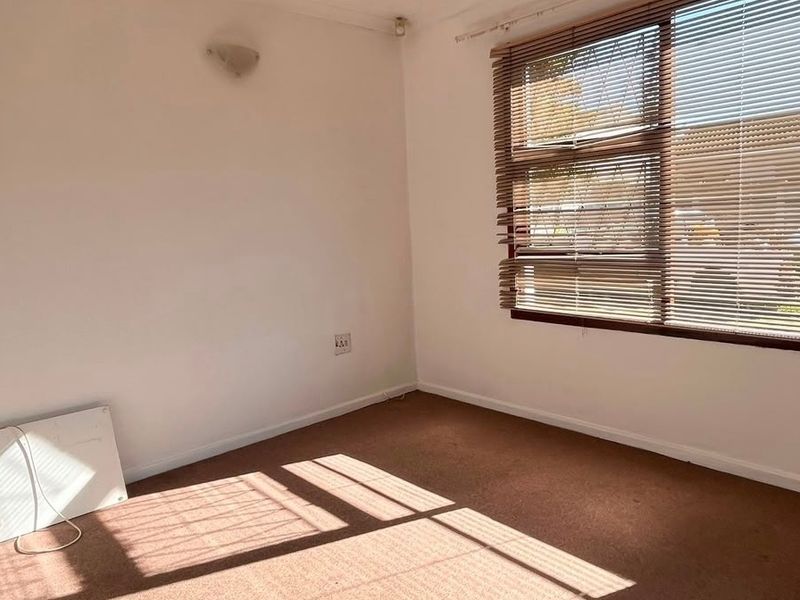 A vacant bedroom featuring carpeted flooring, a wall-mounted light fixture, and a window fitted with venetian blinds.