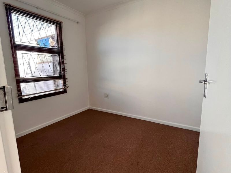 A vacant bedroom featuring carpet flooring, a window with security bars, and a recessed ceiling light.