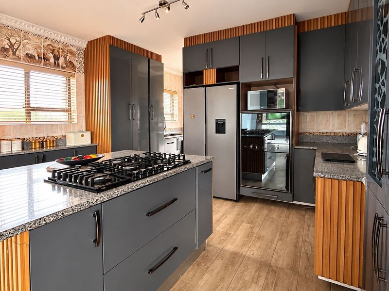 Modern kitchen featuring high-end grey cabinetry, granite countertops, a central island with a gas hob, and integrated appliances with stylish wood slat accents.