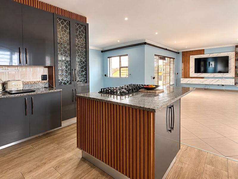 Modern open-plan living area featuring a contemporary kitchen with a central island, gas hob, granite countertops, and a stylish media wall.