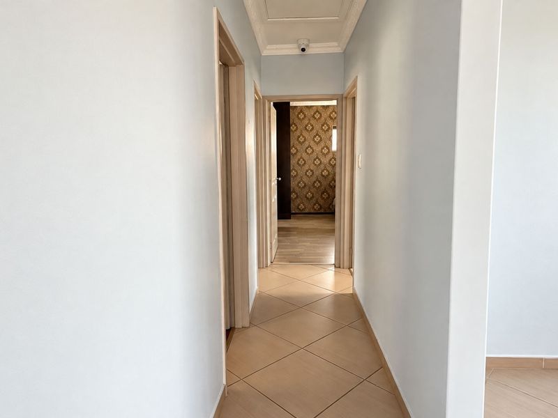 A clean, well-lit hallway featuring neutral tiled flooring and multiple doorways leading to adjacent rooms.