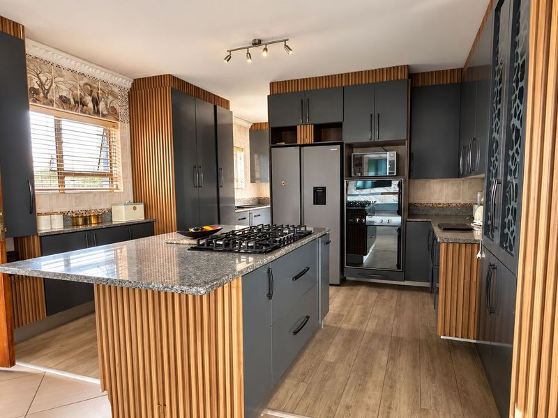Modern kitchen featuring granite countertops, a central island with a gas hob, built-in appliances, and stylish slatted wood cabinetry detailing.