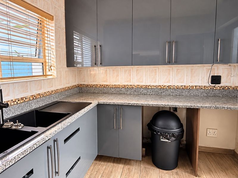 Modern kitchen featuring grey high-gloss cabinetry, granite countertops, and a black composite double sink with a matching gooseneck mixer tap.