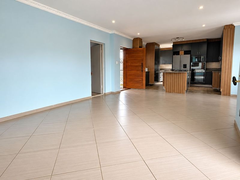 Spacious open-plan living area featuring neutral tiled flooring, recessed lighting, and a modern kitchen with built-in cabinetry and integrated appliances.
