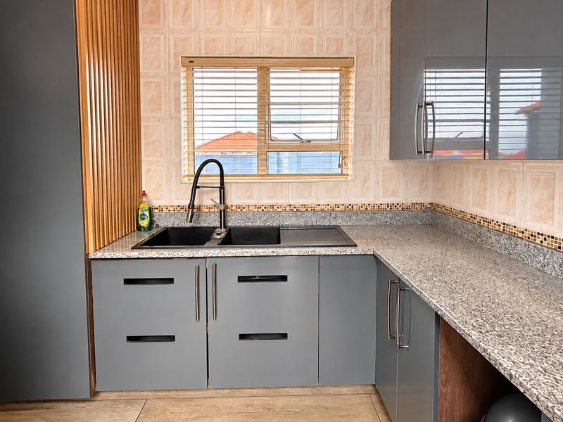 A modern kitchen featuring grey cabinetry, granite countertops, a double basin sink with a contemporary mixer tap, and a decorative slatted wood feature wall.