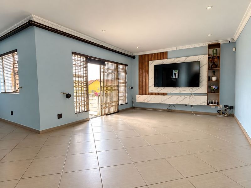 Spacious living room featuring tiled flooring, recessed lighting, crown molding, and a modern built-in media unit with marble-effect detailing.