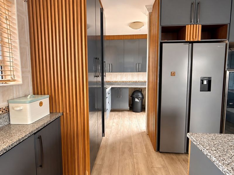 Modern kitchen featuring grey cabinetry, granite countertops, and distinctive slatted wood wall paneling, creating a contemporary and functional cooking space.