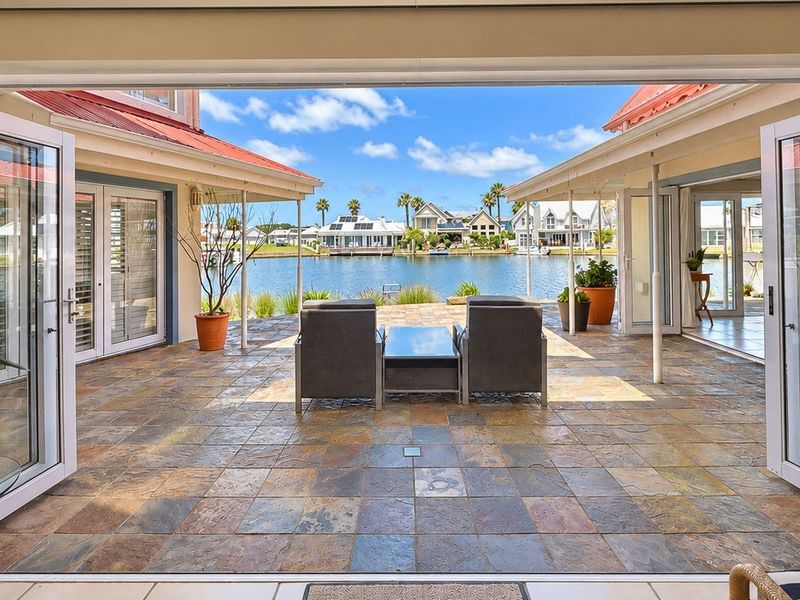 A spacious covered patio featuring durable tiled flooring and wide bi-fold doors, offering seamless indoor-outdoor flow and direct views of the waterfront.