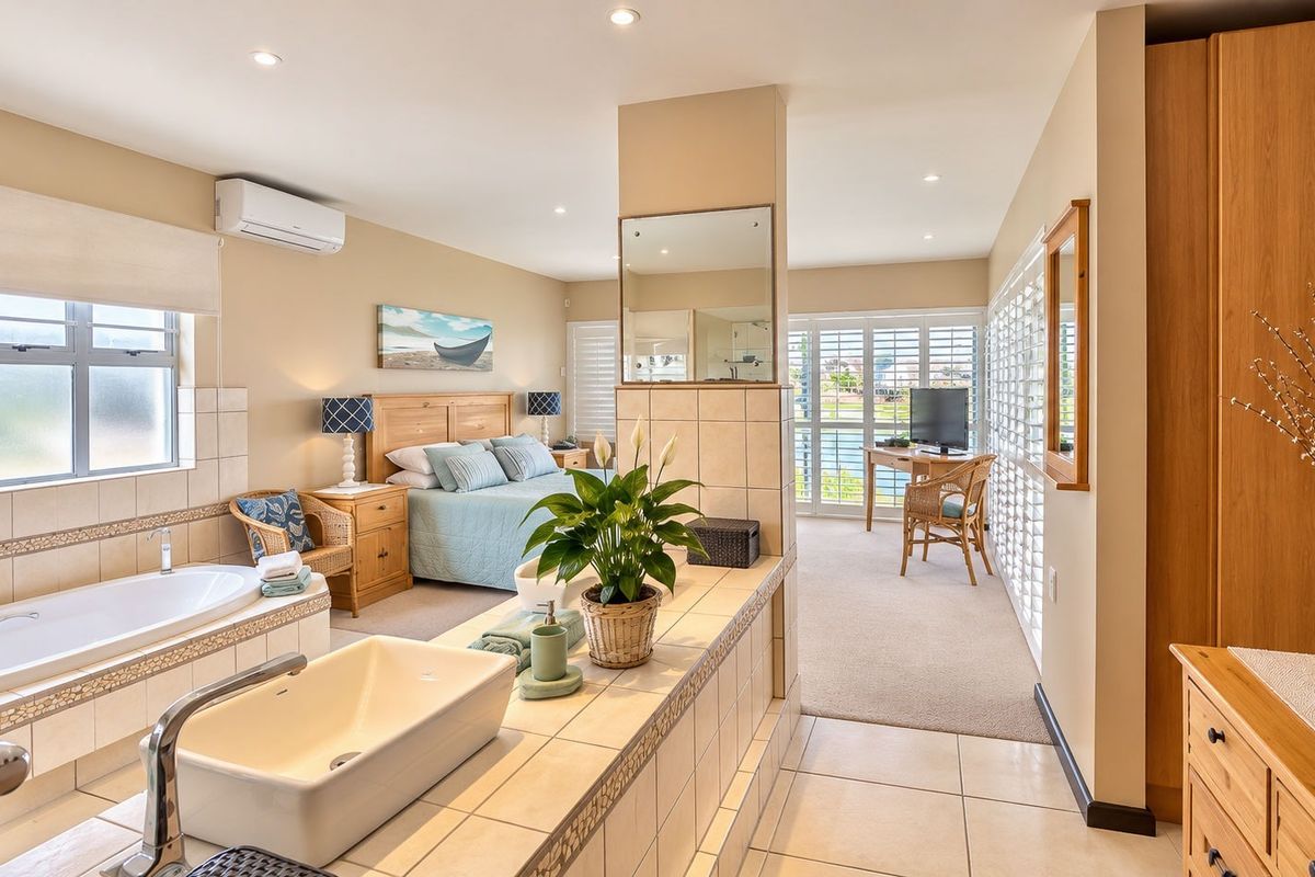 Spacious open-plan bedroom suite featuring an integrated bathroom area with a built-in bathtub, vessel sink, and large windows with plantation shutters.