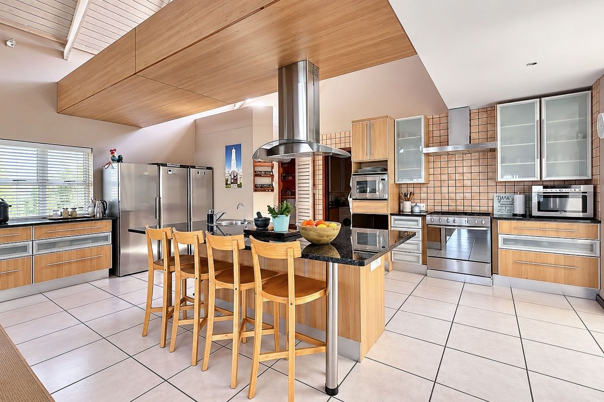 Spacious modern kitchen featuring timber cabinetry, granite countertops, a central island with breakfast bar, and high-quality stainless steel built-in appliances under a vaulted ceiling.