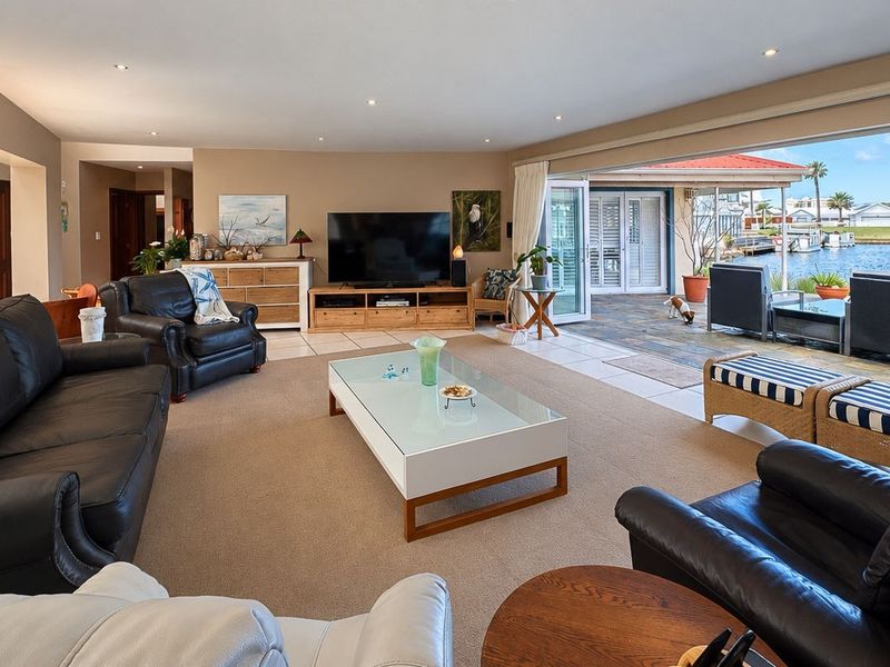 Spacious open-plan living area featuring recessed lighting and large stacking glass doors that open onto a tiled patio with waterfront views.