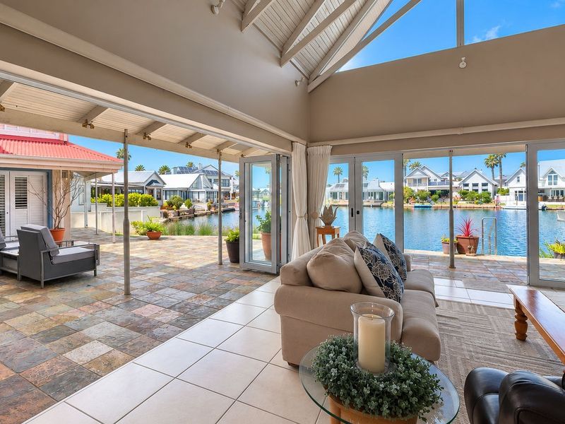 Spacious open-plan living area featuring vaulted ceilings and seamless indoor-outdoor flow through bi-fold doors to a covered patio overlooking the waterfront.