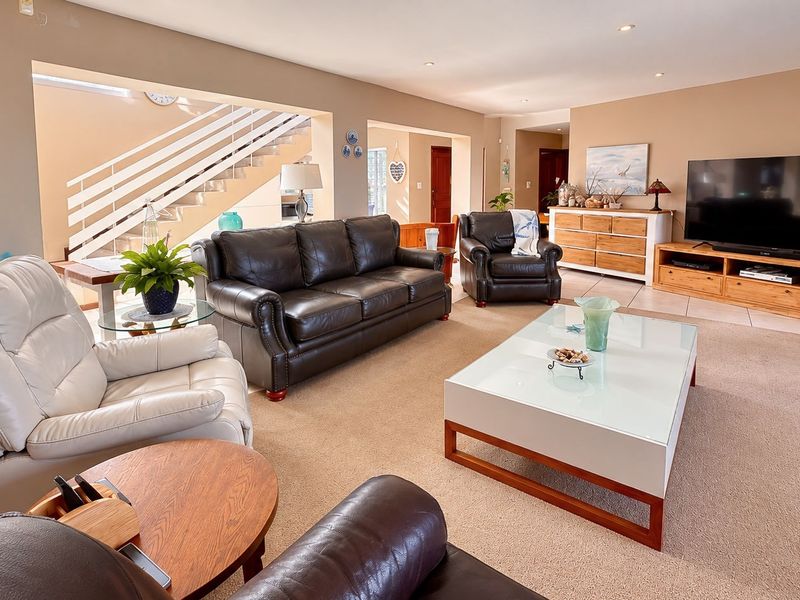 Spacious open-plan living area featuring neutral wall tones, recessed lighting, and a staircase with a white balustrade, creating a bright and inviting atmosphere.