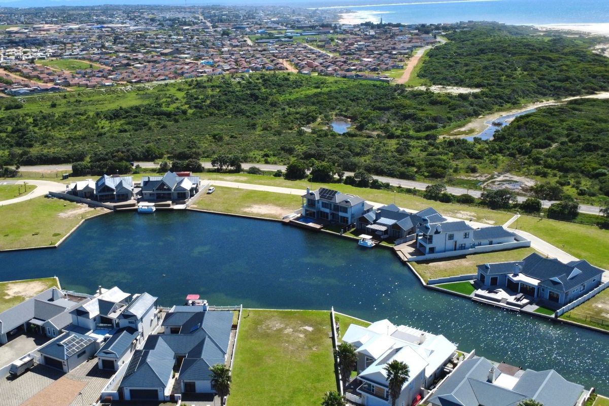 An aerial view of a residential estate featuring modern homes situated along a private canal with coastal surroundings.