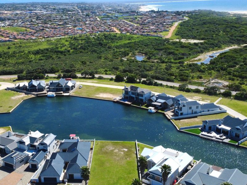 An aerial view of a residential estate featuring modern homes situated along a private canal with coastal surroundings.